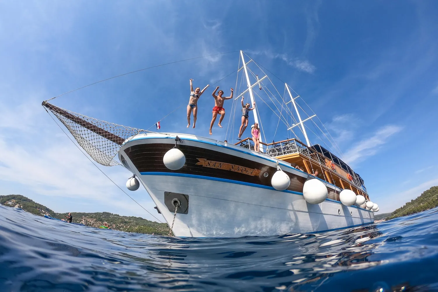 Enthusiastic children and teenagers jumping into the crystal-clear Adriatic Sea directly from the bow of the San Snova motor yacht.