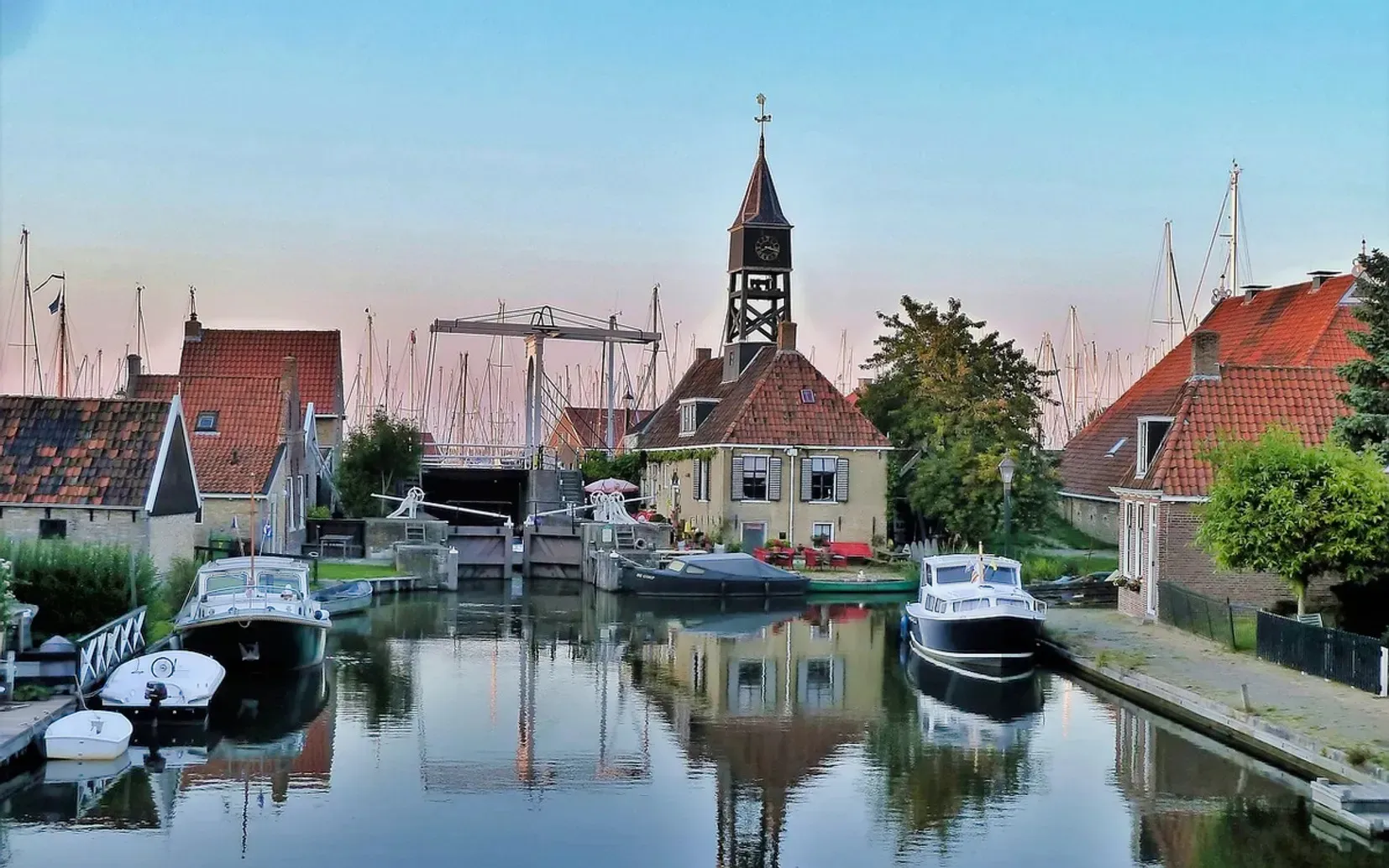Charming Dutch village canal scene featuring a historic lock keeper house, drawbridge, and moored boats
