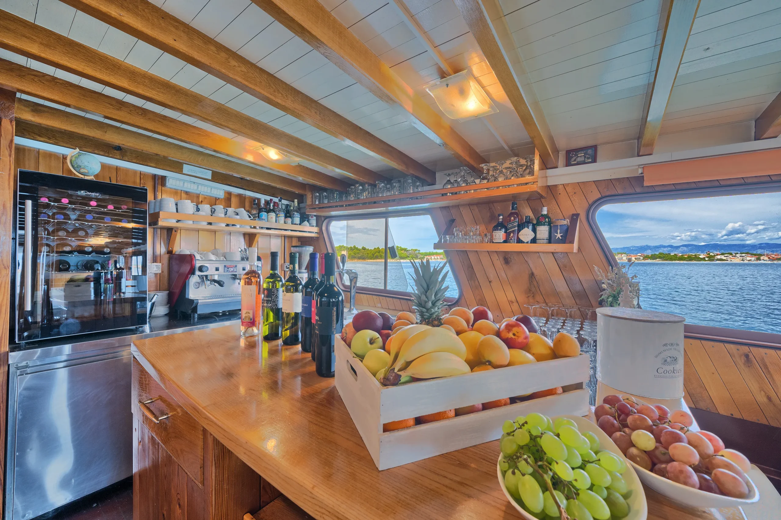 Wooden bar counter with wine bottles, fresh fruit basket, and coffee machine inside MS Linda.