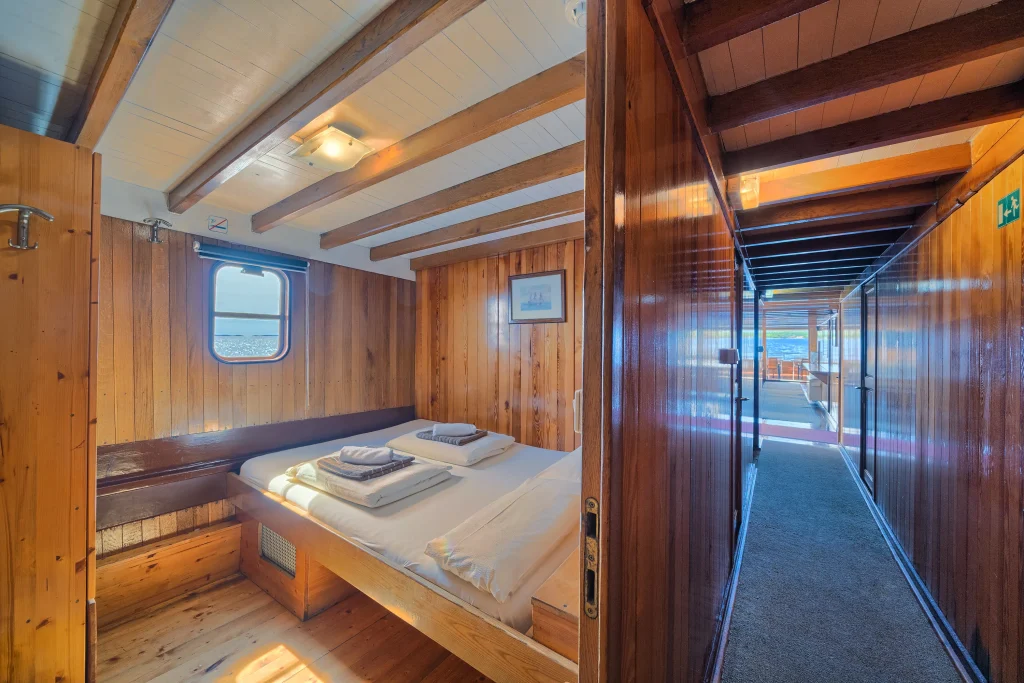 Wooden double cabin on the main deck of MS Linda with a window showing the ocean.