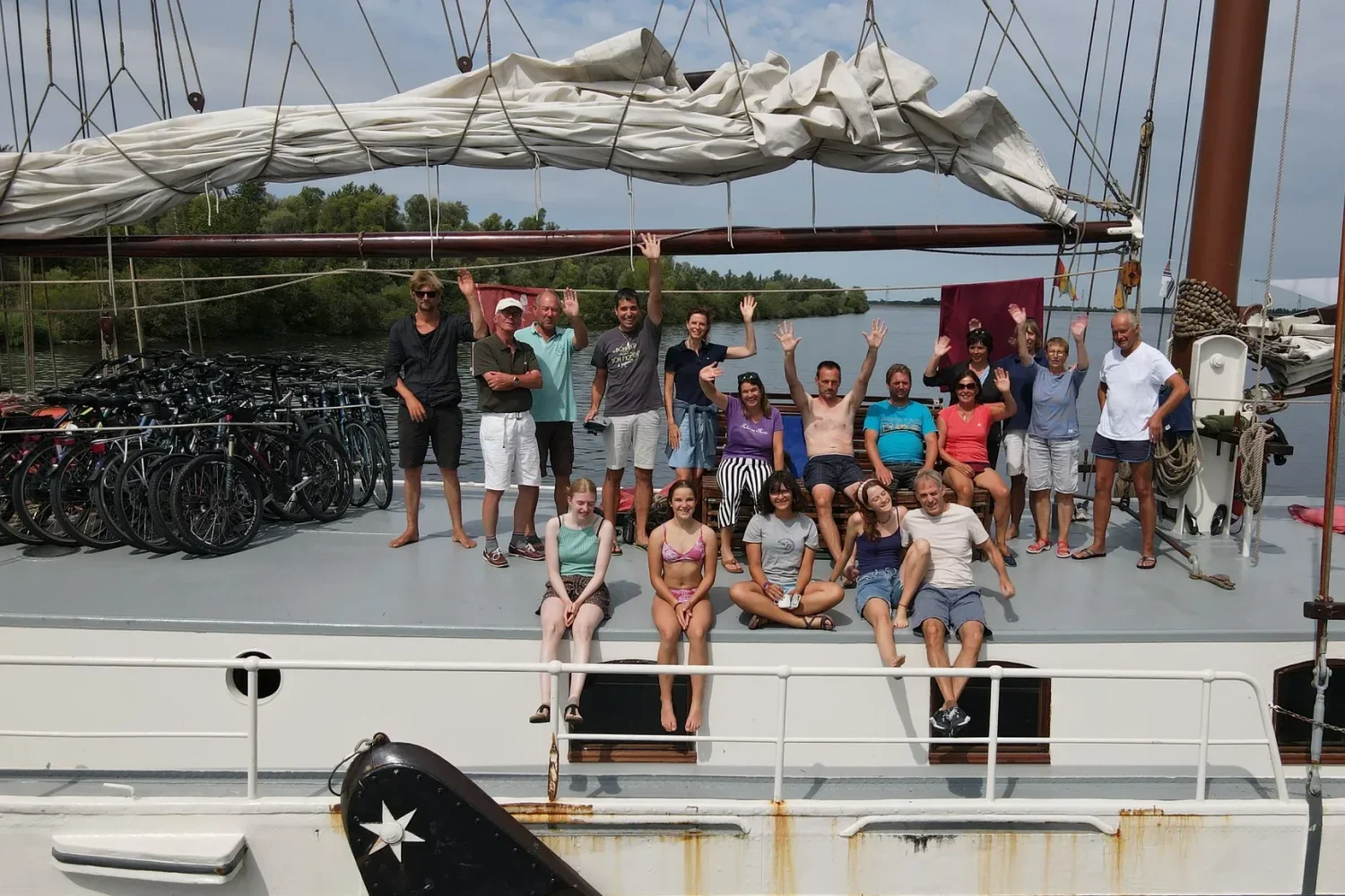 Happy group of tour passengers and crew waving from the deck of a historic three-masted sailing ship