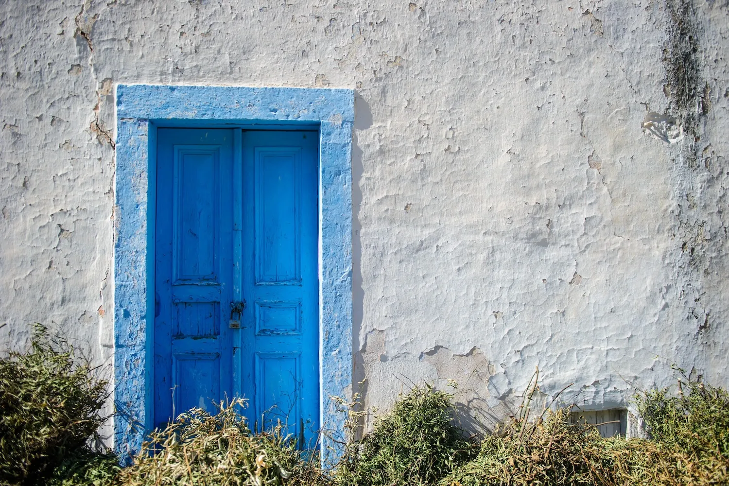 Classic white-washed Cycladic building with a vibrant blue wooden door frame and traditional stone accents on a sunny Greek island.