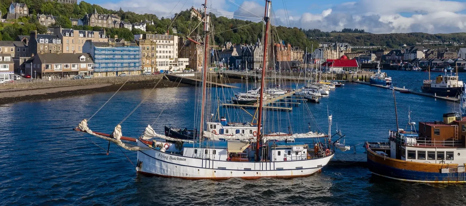 The traditional tall ship Flying Dutchman anchored in the scenic harbour of Oban with McCaig's Tower in the background.